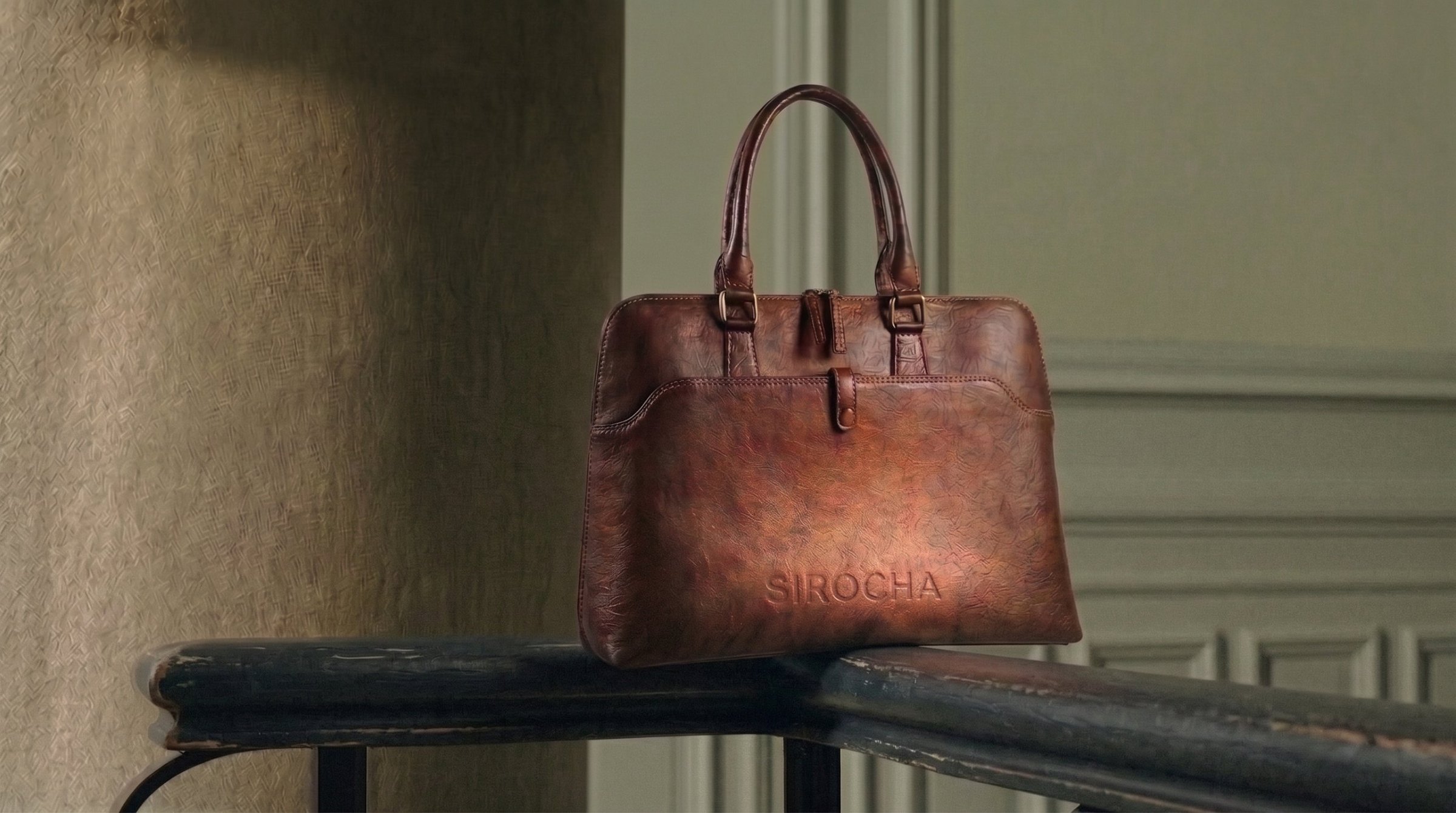 SIRÓCHA brown leather bag with embossed logo, resting on a railing